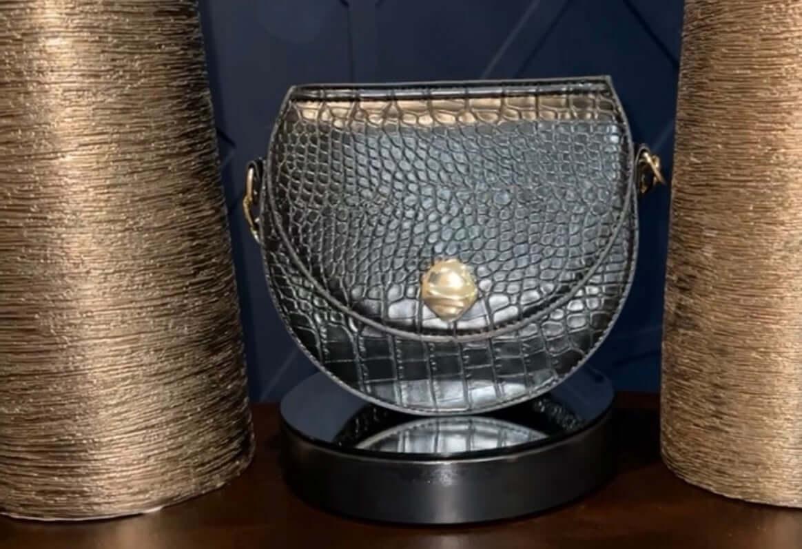 Black crocodile embossed leather handbag with gold clasp, displayed between gold textured vases