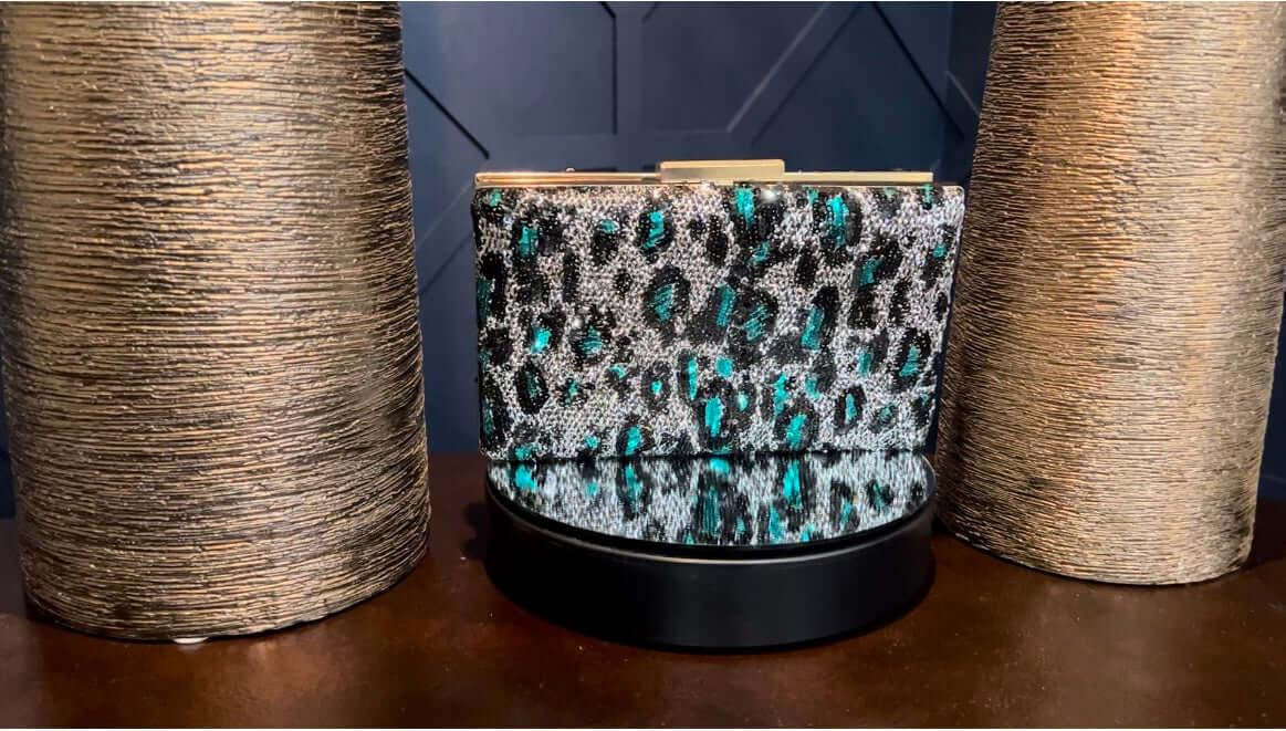 Sparkly turquoise leopard print clutch purse displayed between two textured gold vases.
