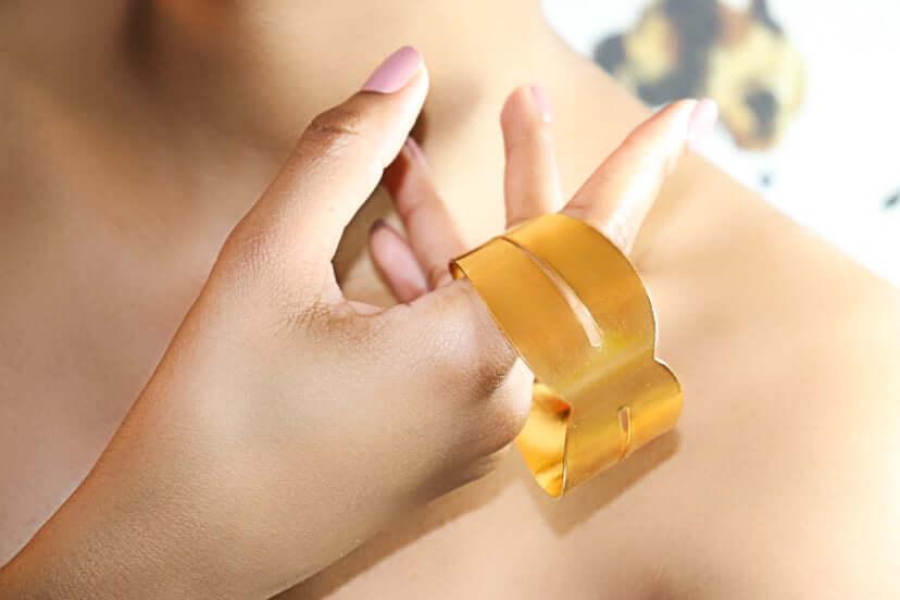 Hand wearing modern gold cuff bracelet against bare skin and soft lighting
